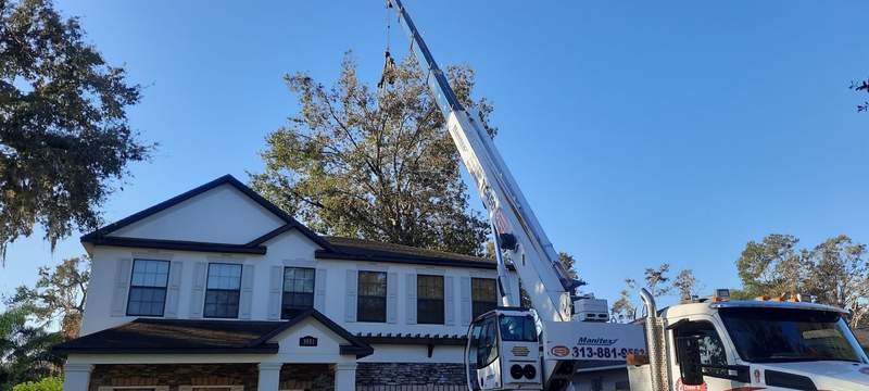 Crane boom reaching high beside a two-story home during a tree job.