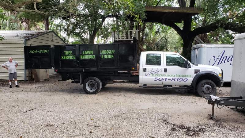 Andy's PGM crew-cab dump truck with 504-8190 on the door, parked in a gravel yard beside a shed.