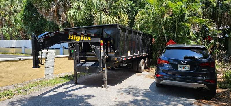 Large black gooseneck dump trailer backed into a residential driveway.