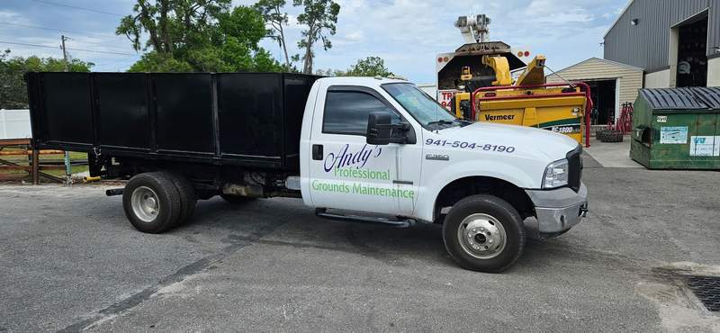 Andy's PGM dump truck with 941-504-8190 on the door, a wood chipper parked behind it.