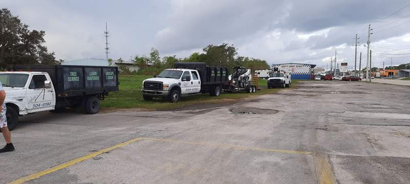 Andy's PGM trucks lined up in a parking lot: dump trucks, a trailer carrying a track loader, and a bucket truck.